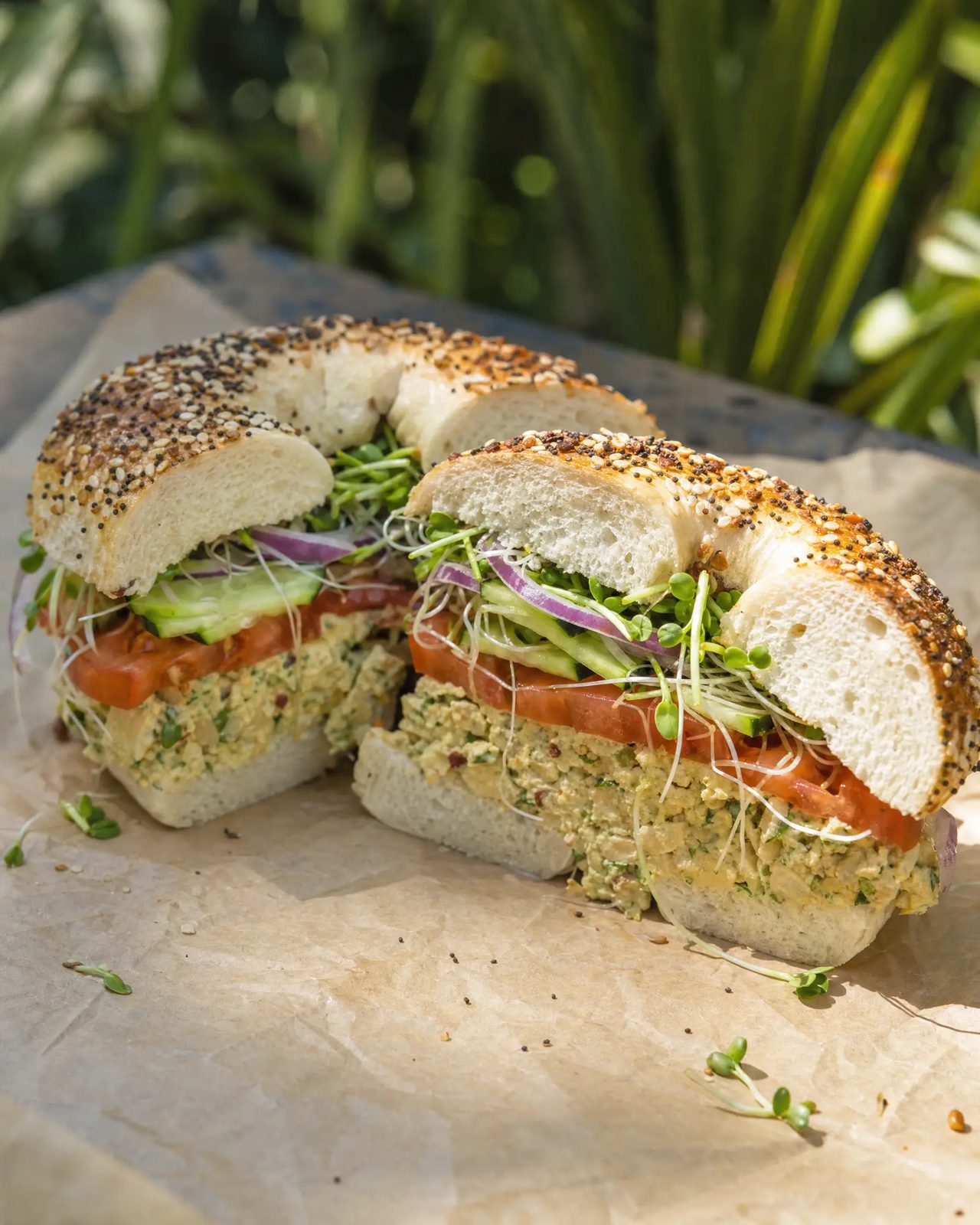 Loaded bagel sandwich stacked with smashed chickpea filling and fresh vegetables