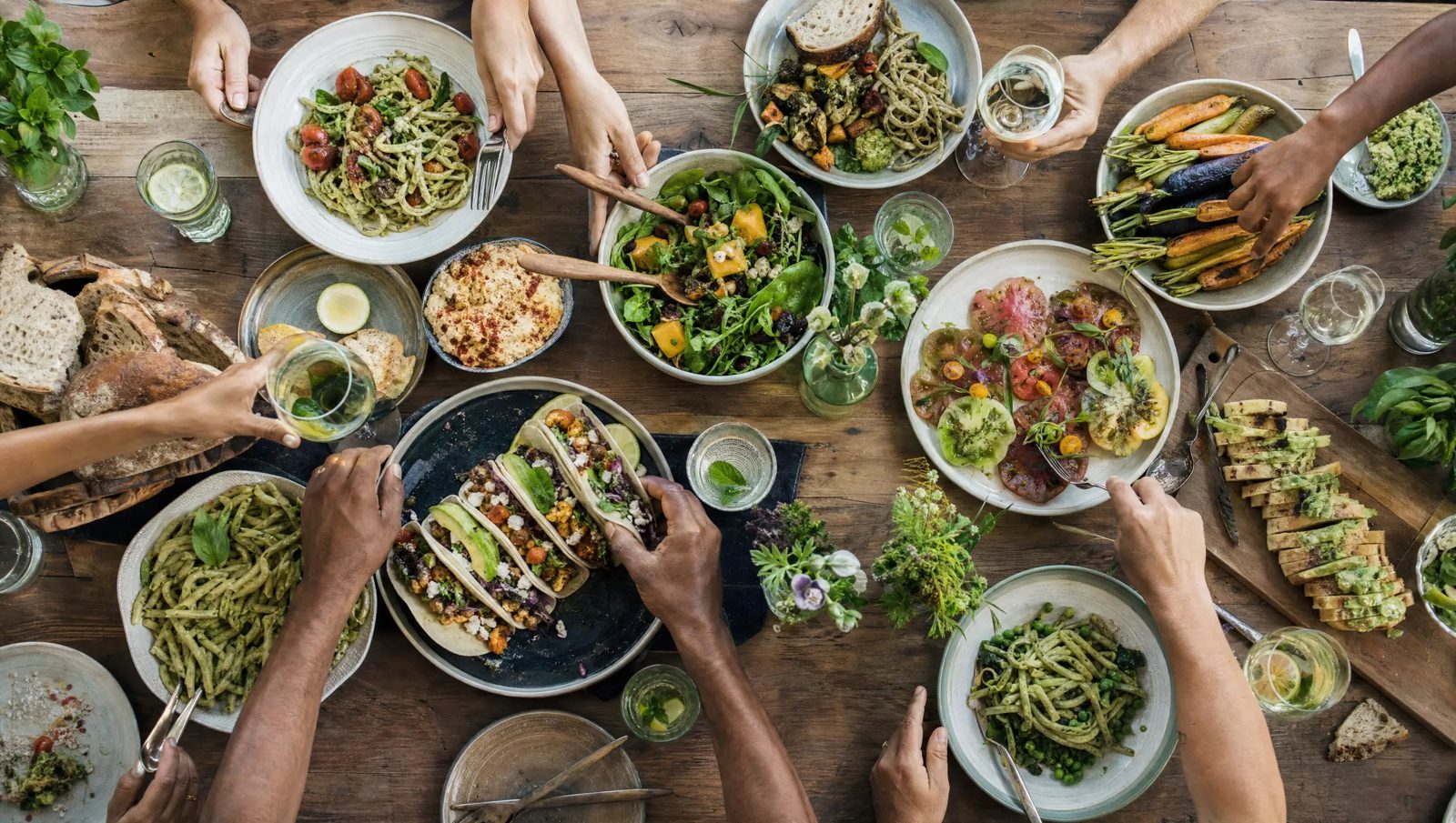Overhead view of many hands sharing vegan dishes around a table
